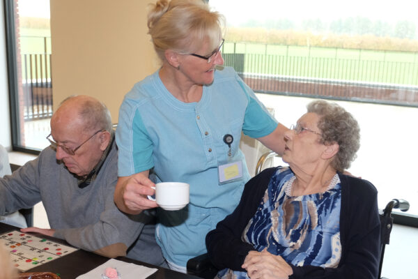 Een medewerkster van woonzorgcentrum Berkenhof in Heers brengt een kopje koffie naar een bewoner die aan een tafel zit in haar rolstoel.